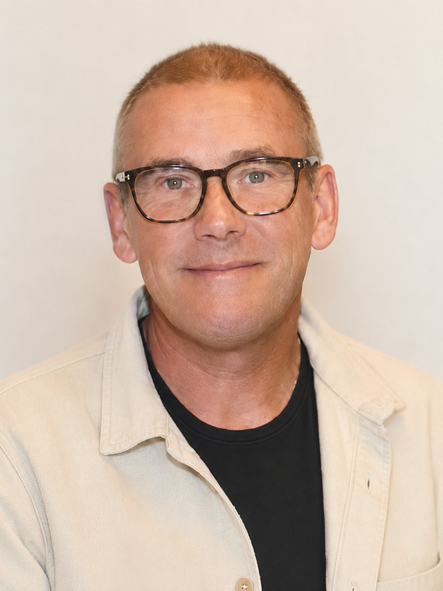 Michael Woods, smiling, wearing glasses and a light jacket